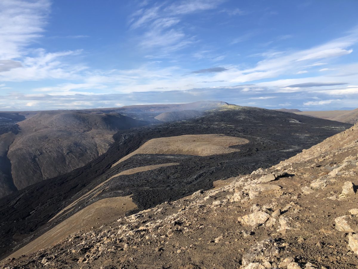 Der Vulkankrater im Hintergrund dampft noch, die schon schwarzen Lavaströme ebenfalls Vulkankrater auf Island mit schwarzer Lava