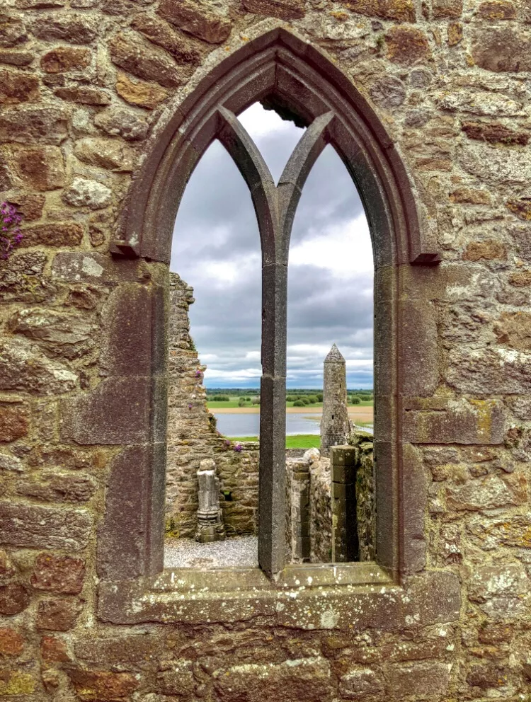 Irland Roadtrip: Blick durch eines der erhaltenen Fenster von Clonmacnoise auf die Ruinen und den Shannon River